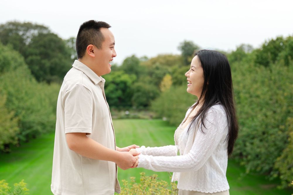 A couple holds hands and smiles at each other in a lush green outdoor setting.