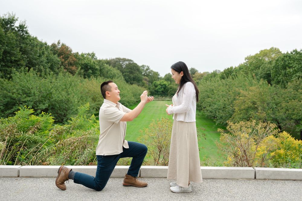 Man proposing on one knee to woman outdoors in lush green park setting.