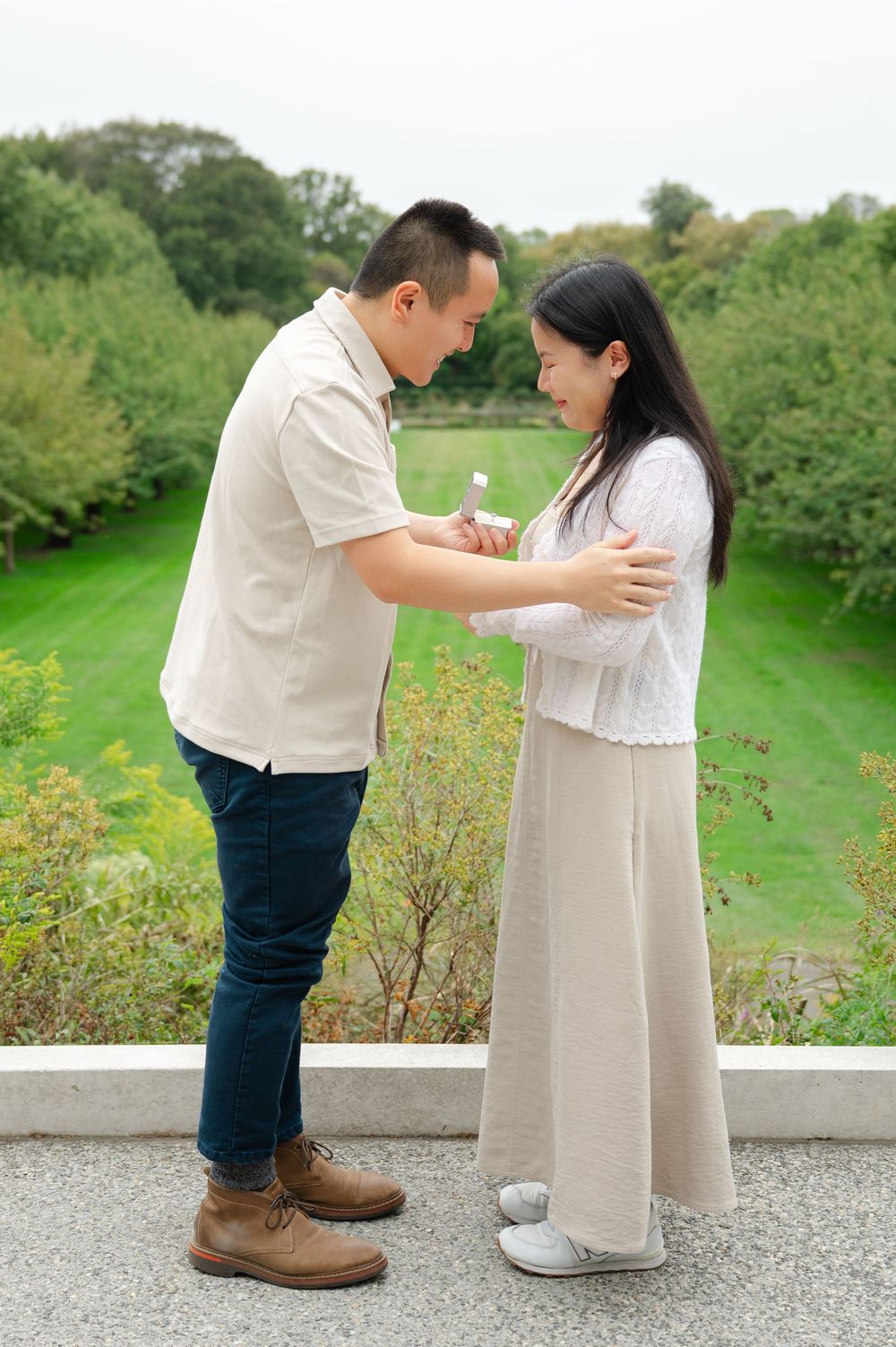 Man presenting ring to surprised woman during outdoor marriage proposal in park.