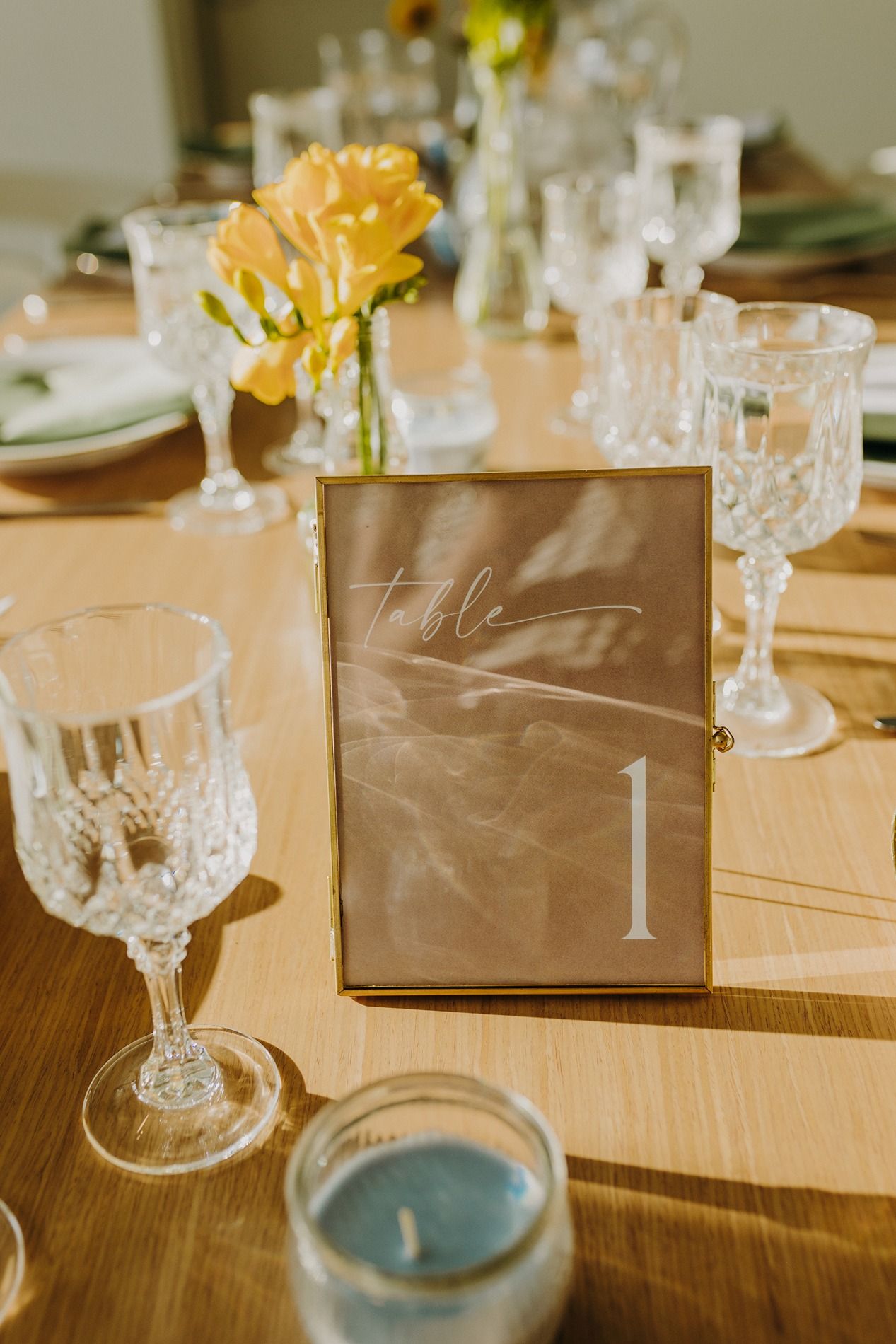 Elegant wedding table setting with crystal glasses, yellow flowers, and a gold-framed Table 1 sign on a wooden table at The Lane.