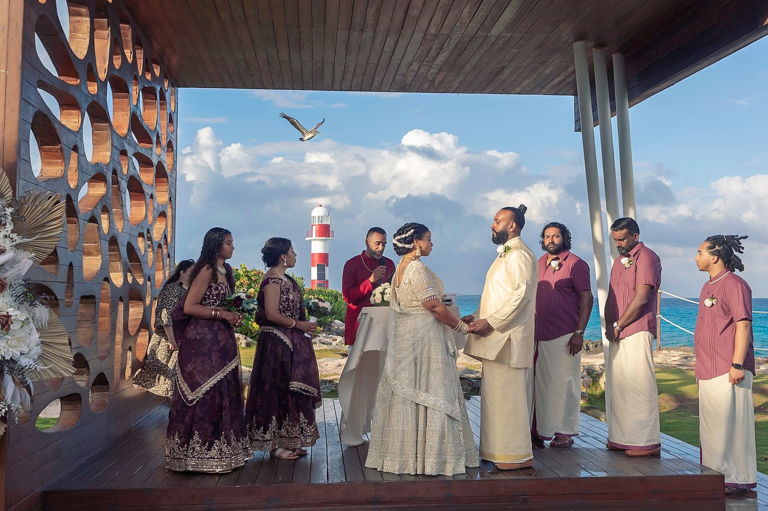 A wedding ceremony taking place outdoors at a waterfront venue with scenic views of a lighthouse and blue sky.