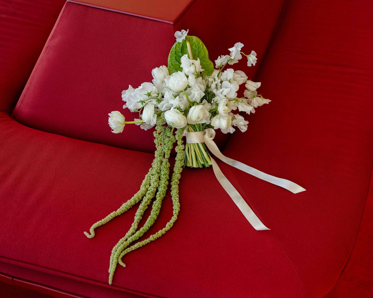 Elegant white lily of the valley and rose wedding bouquet displayed on red velvet seating.