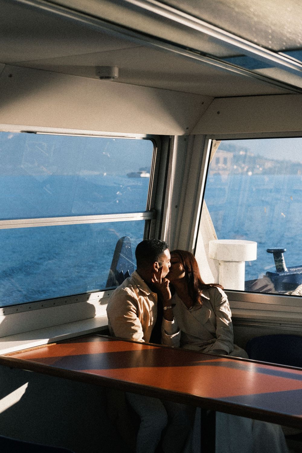 Person looking out window of ferry boat crossing blue waters on sunny day.