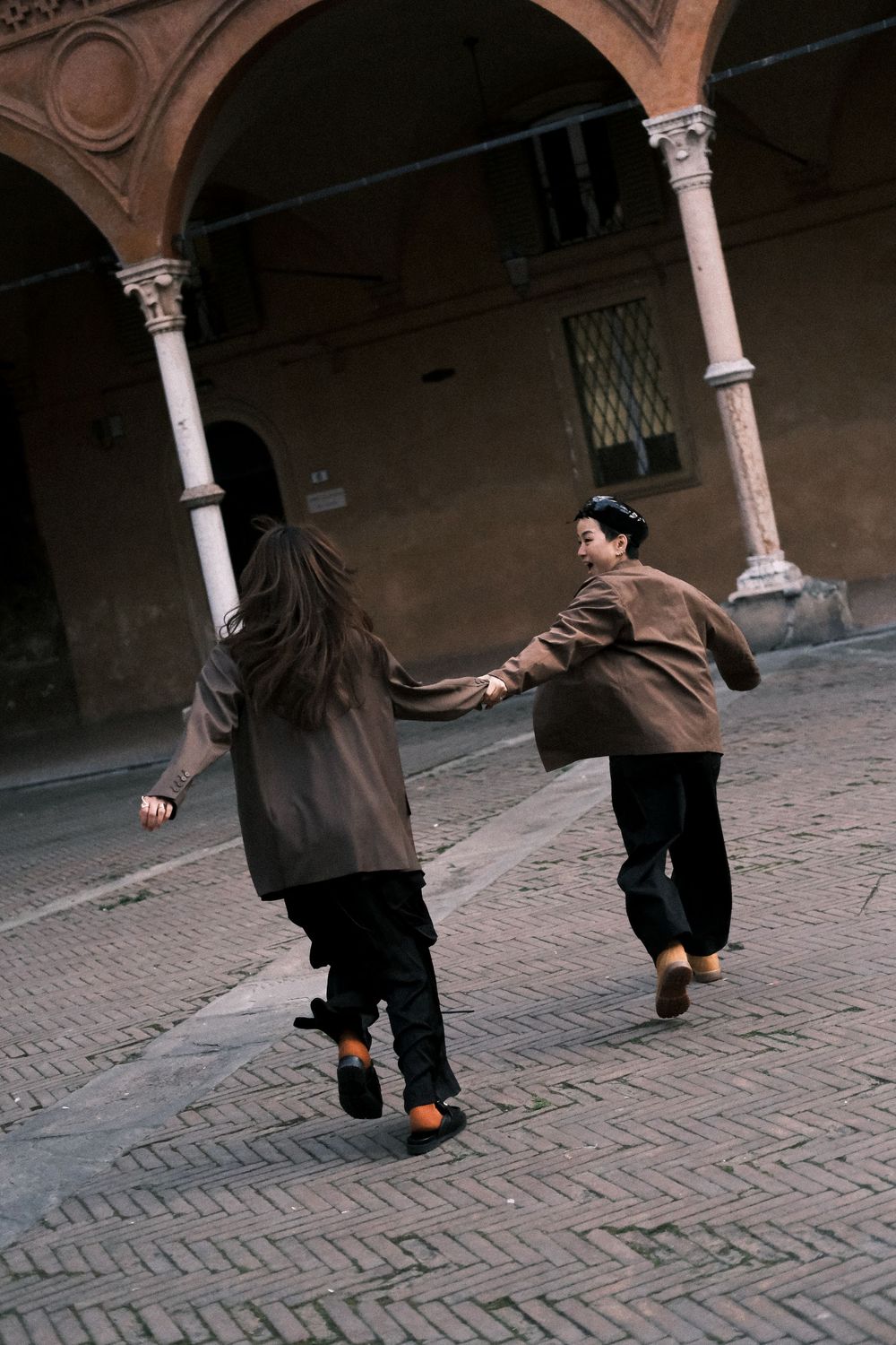 Couple running hand-in-hand through historic streets of Bologna during a candid destination engagement photo shoot