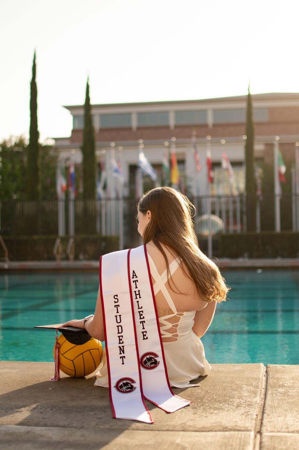Female student athlete sits poolside with water polo ball wearing Student Athlete sash.