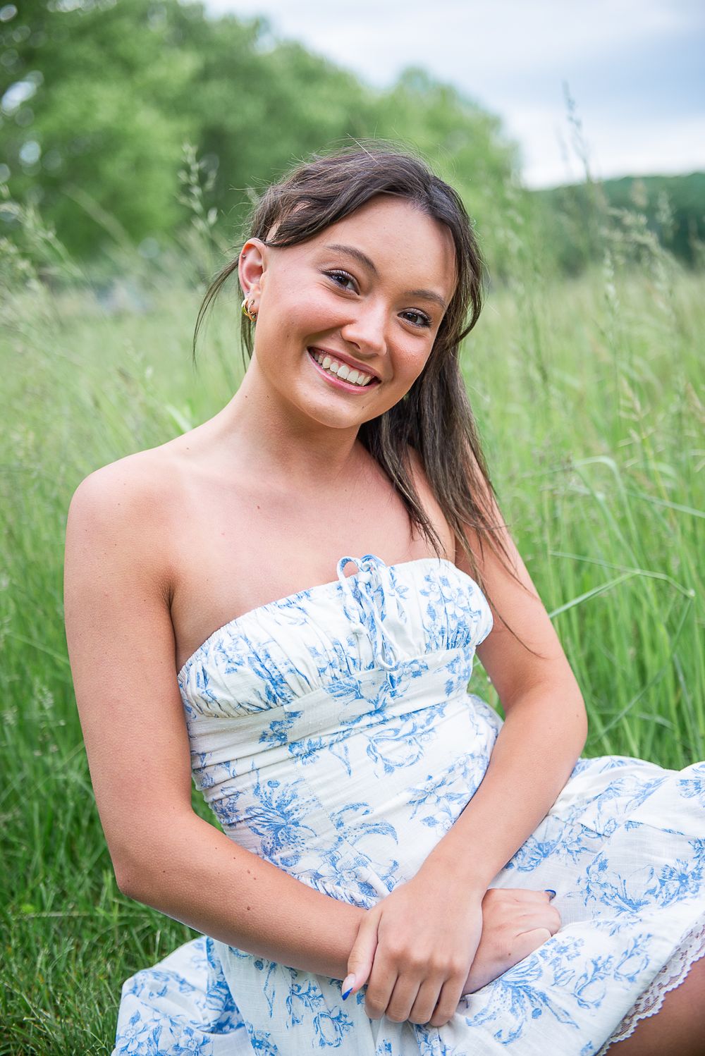 Natural portrait in blue and white floral dress against green summer meadow.