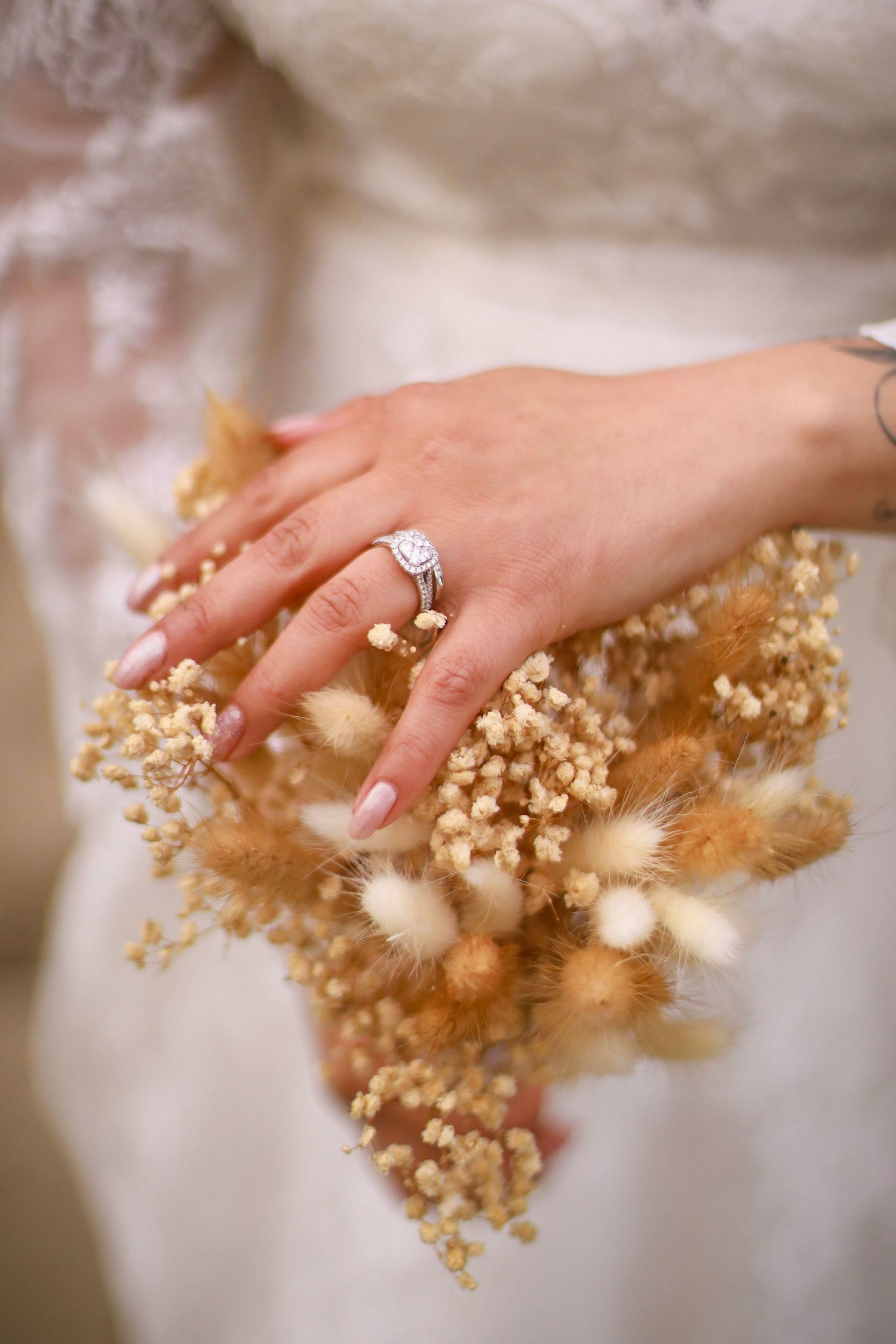 Close up of bride's hand with engagement ring holding dried flowers and pampas grass.