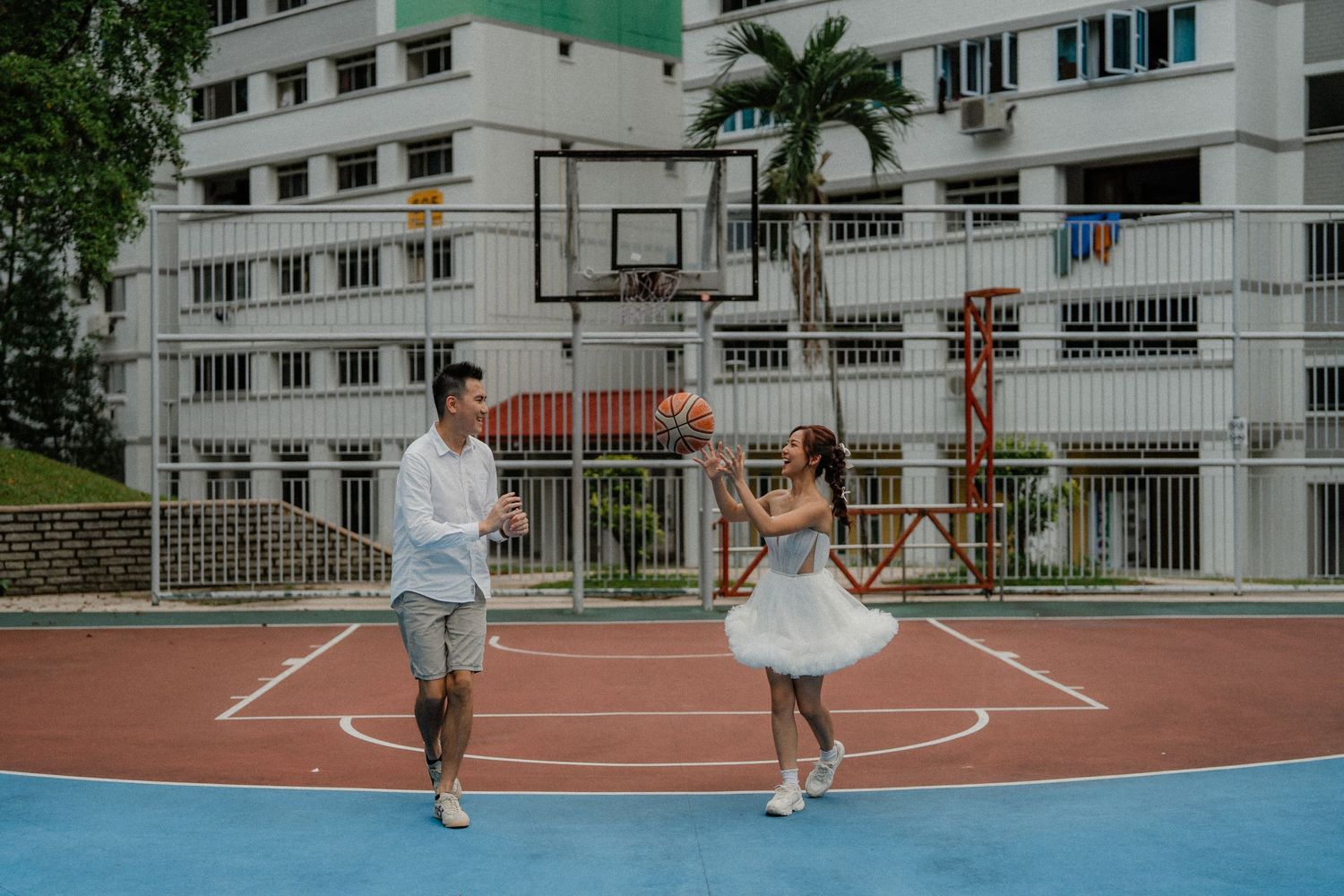 A playful couple dances with a basketball on an outdoor court in an urban setting.