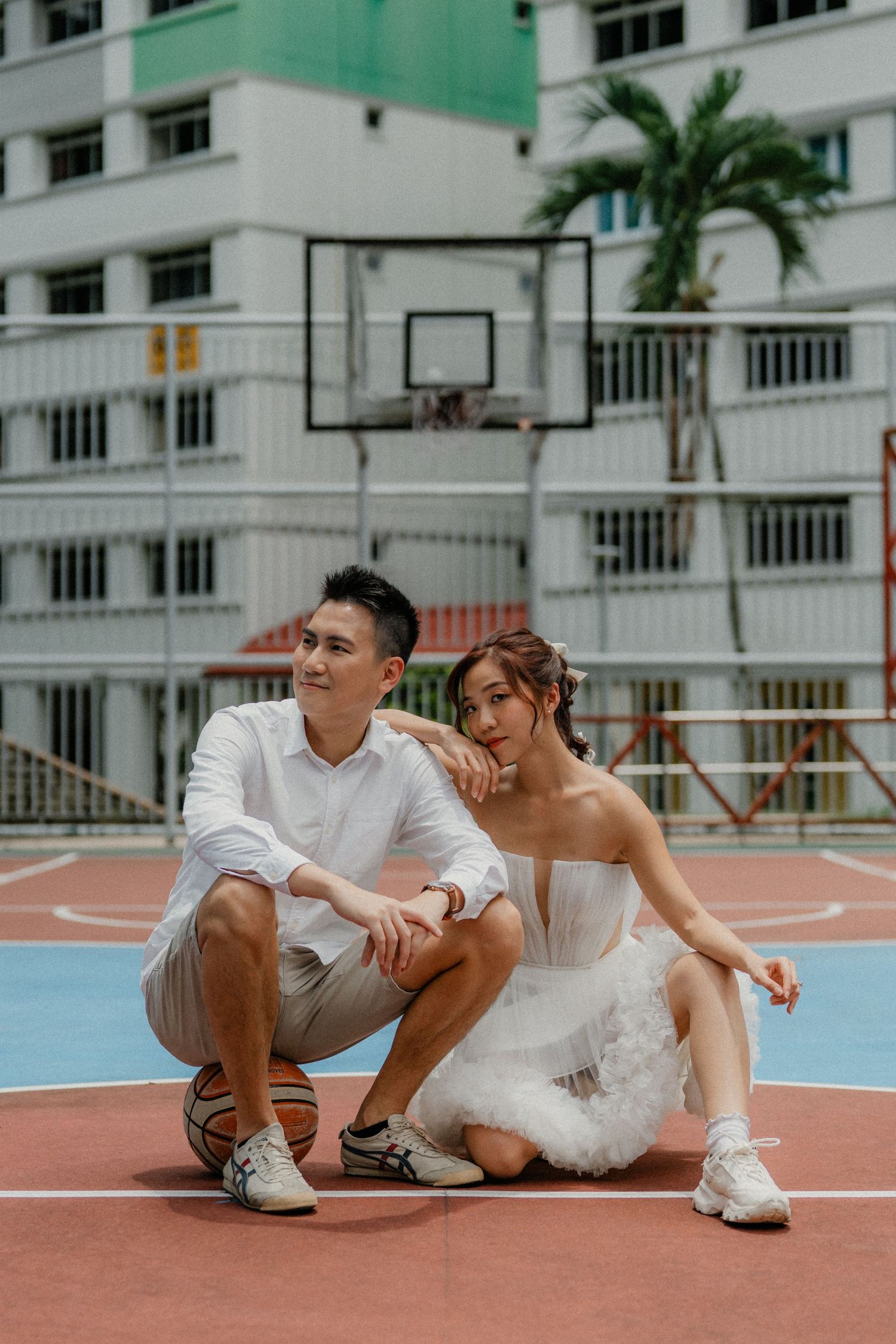 Two people in white outfits sit together on a blue and red basketball court surface.