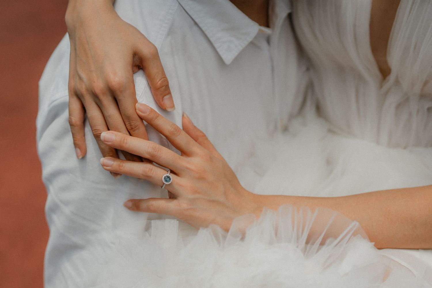 Close-up details of white wedding dress fabric and delicate hands with an engagement ring.