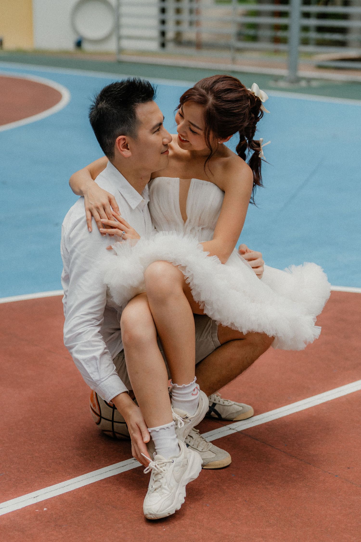 A tender moment between newlyweds sitting on an outdoor basketball court.