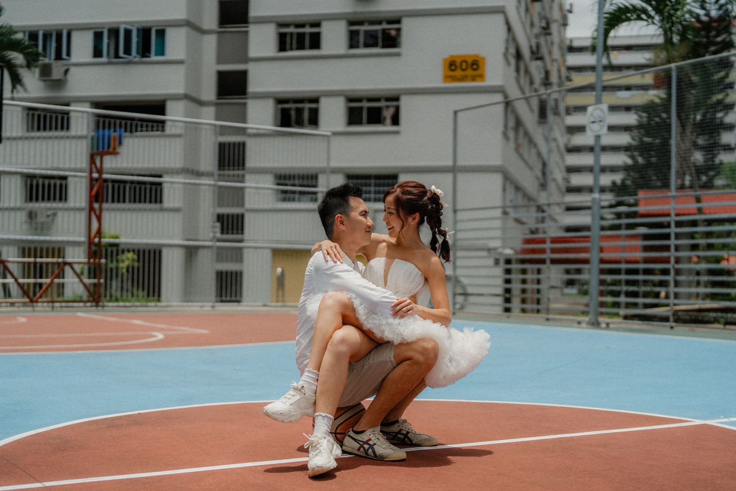 A young couple in casual white outfits sharing a tender moment on an outdoor basketball court.