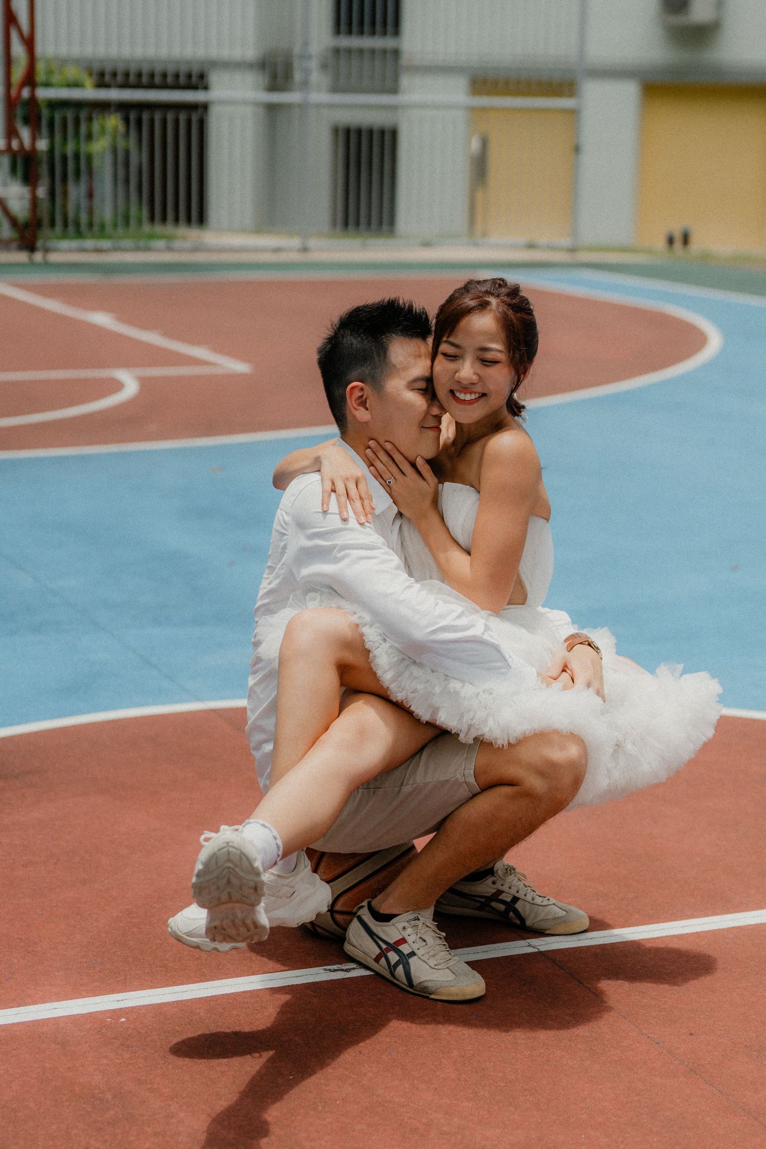 A romantic moment captured on a colorful basketball court with apartment buildings in the background.