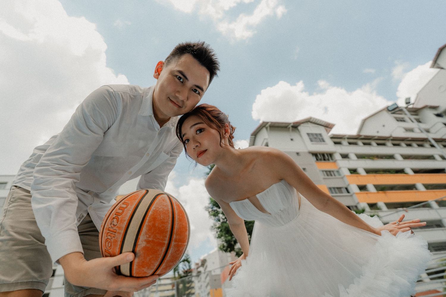 A couple plays with a basketball against a backdrop of urban architecture and blue sky.