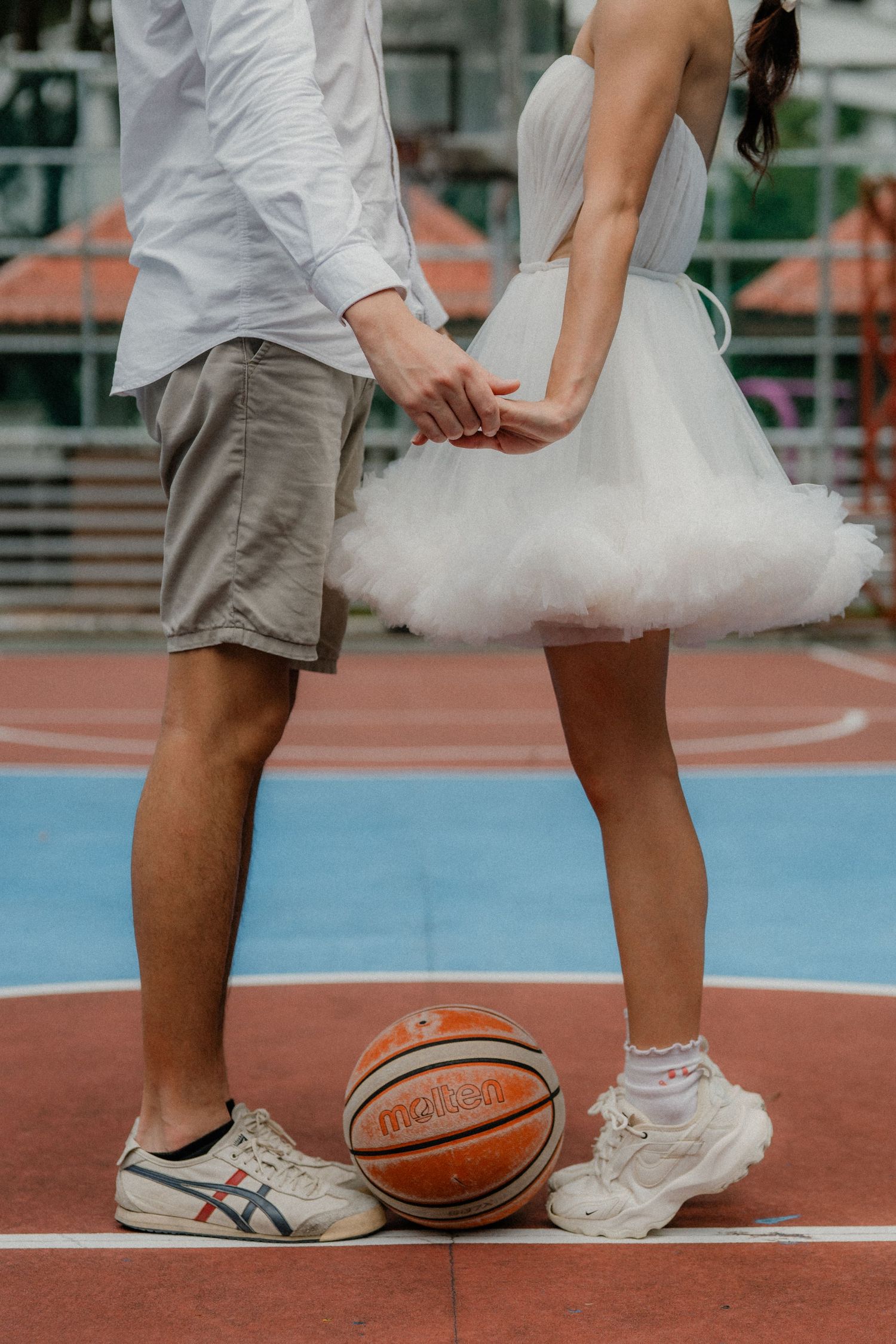 Close-up view of feet in white sneakers and a basketball on an outdoor court.