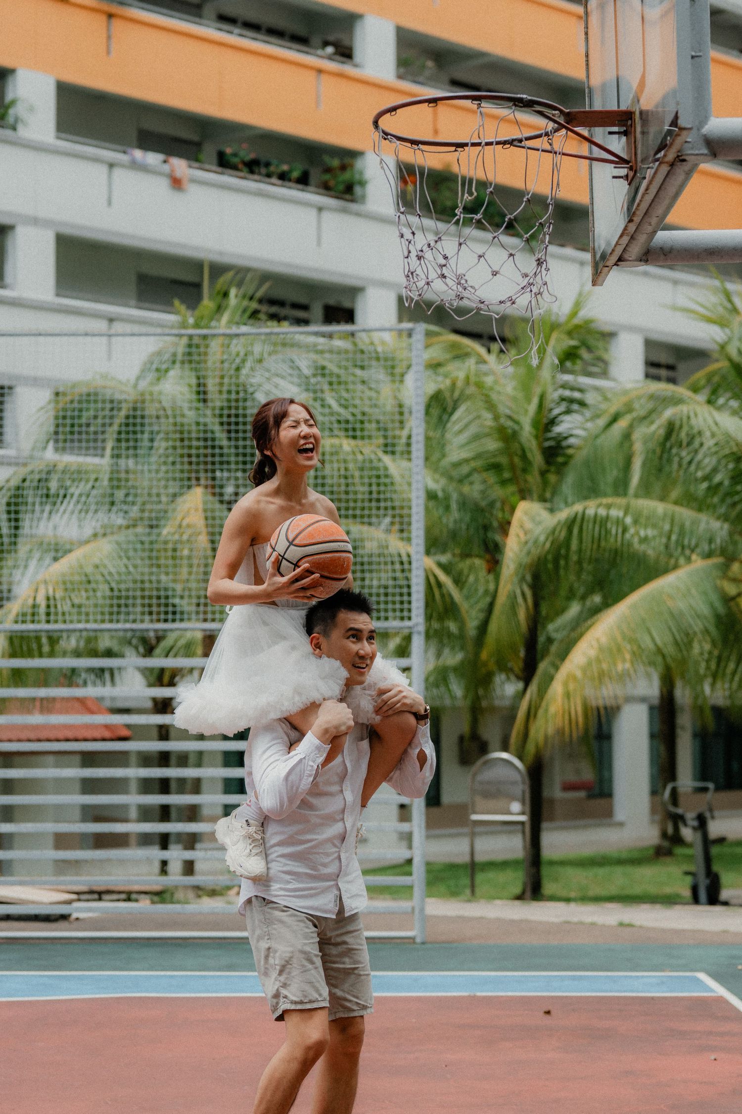 A playful moment on a basketball court as two people have fun with one person sitting on shoulders.