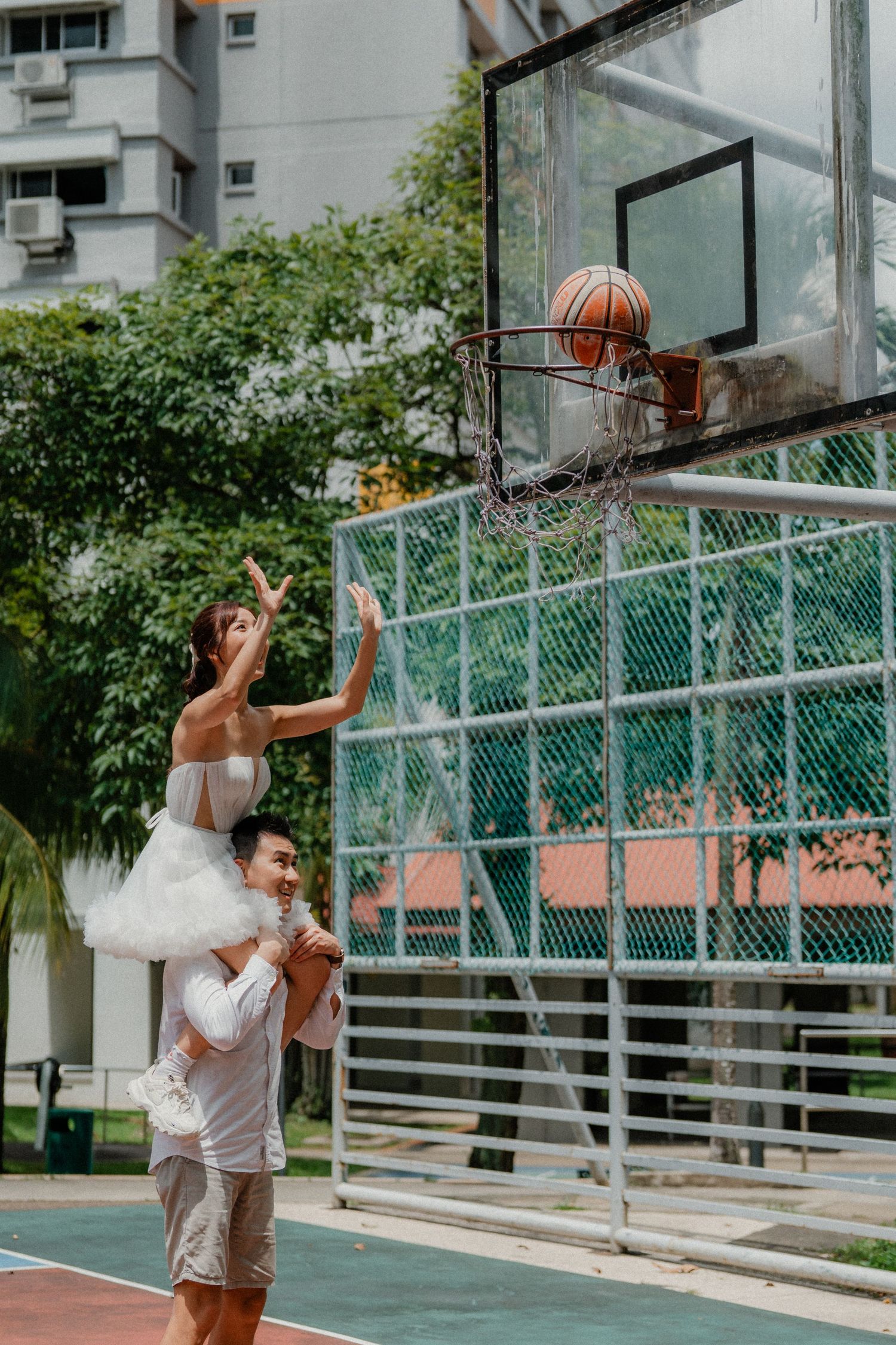 A couple creates a fun basketball-themed wedding photo with the bride reaching for a basket.