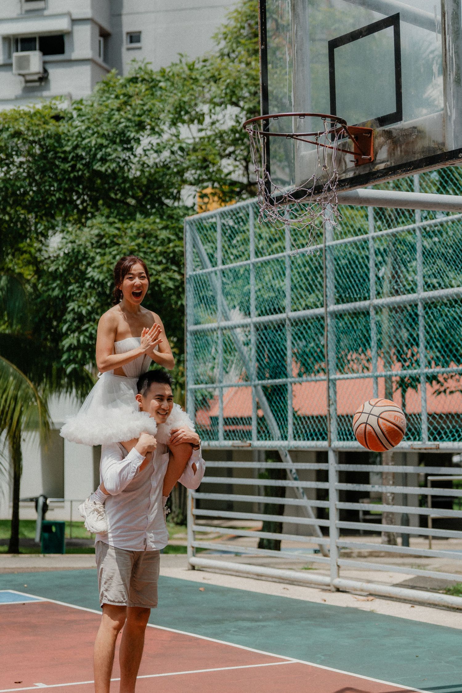 A couple shares a fun moment on a basketball court near an apartment building.