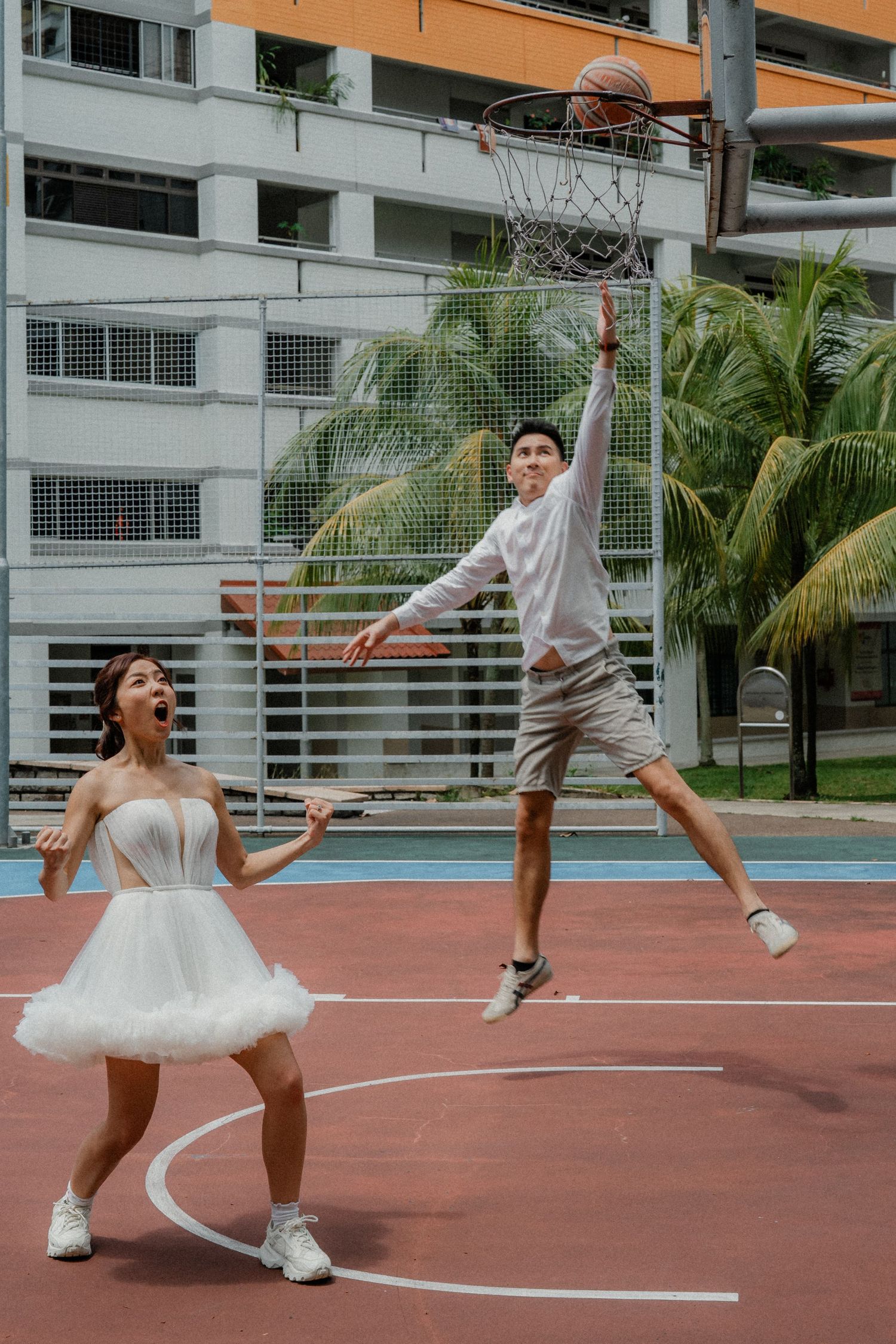 Energetic basketball playing sequence on an outdoor court with white buildings in background.