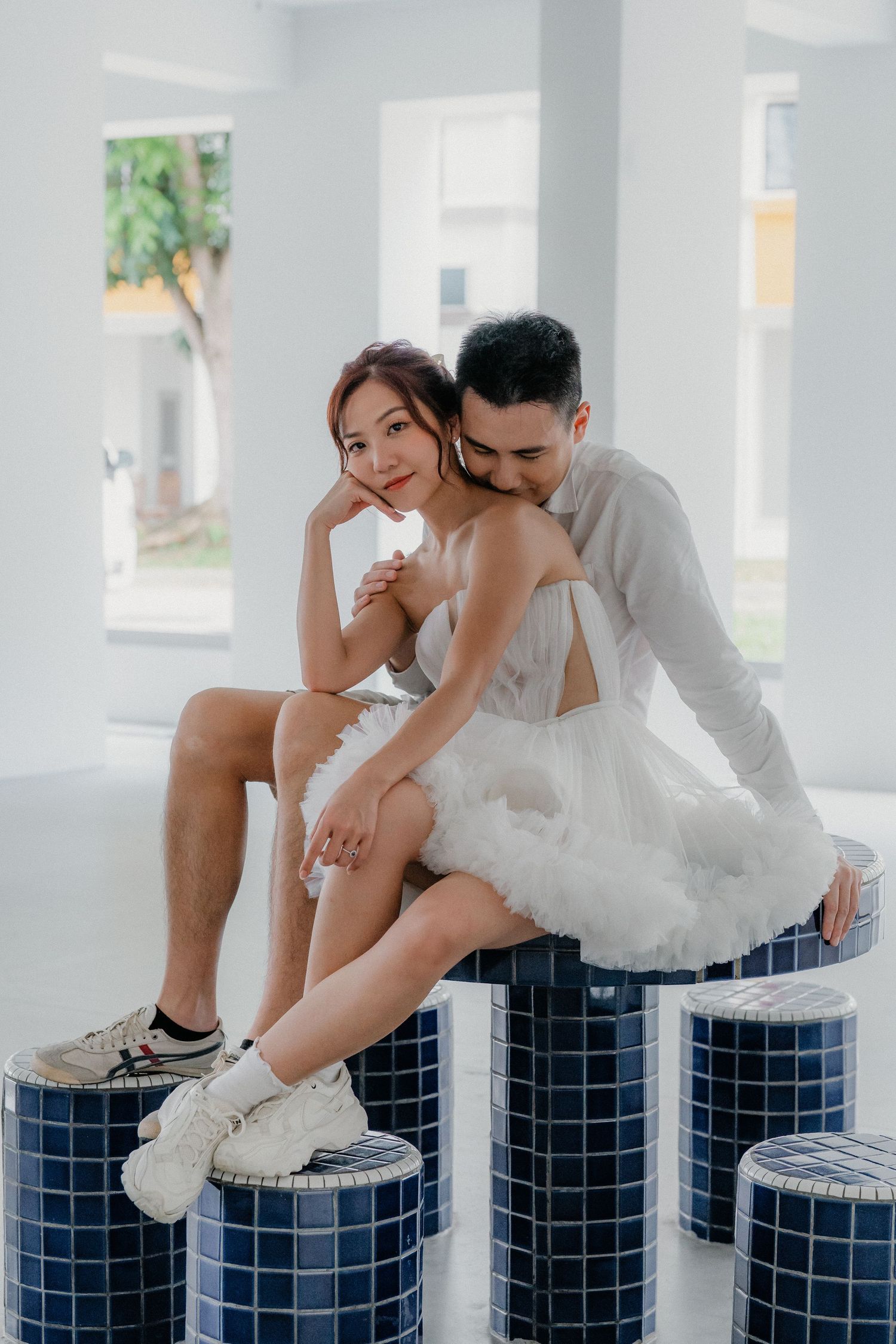 Couple in white clothing sitting together on blue mosaic steps in a bright modern interior.