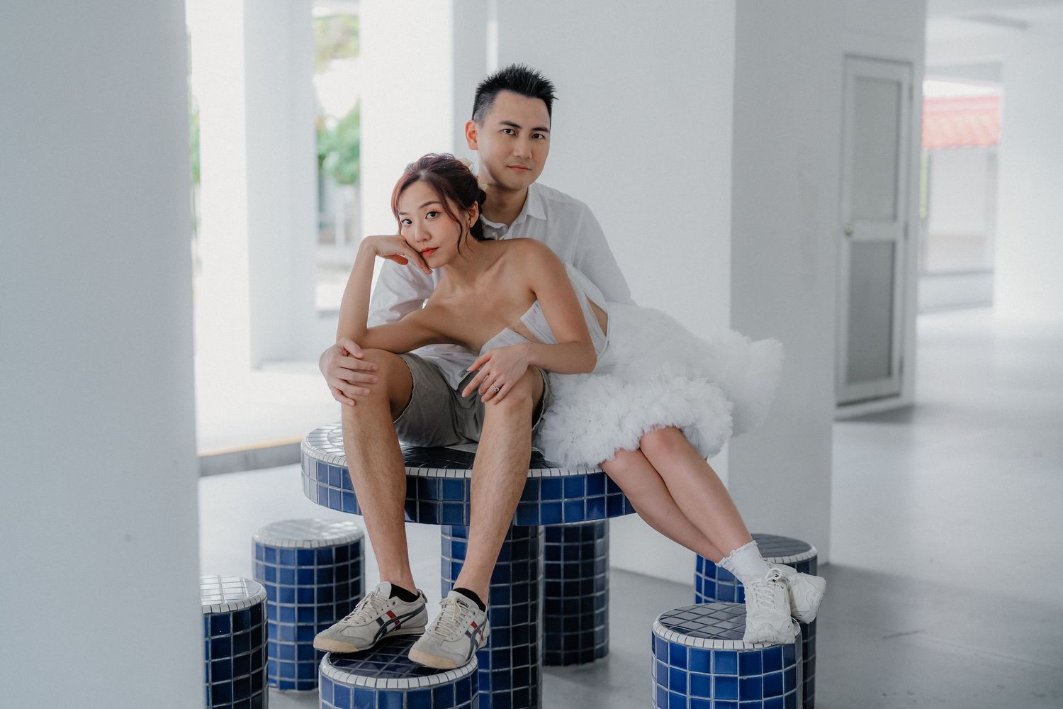 Person in workout attire sits on blue tiled edge of pool wearing white sneakers in contemplative pose.