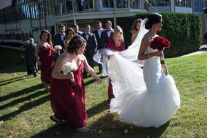 Bridesmaids help keep the bride's dress train off of grass as they walk to the ceremony