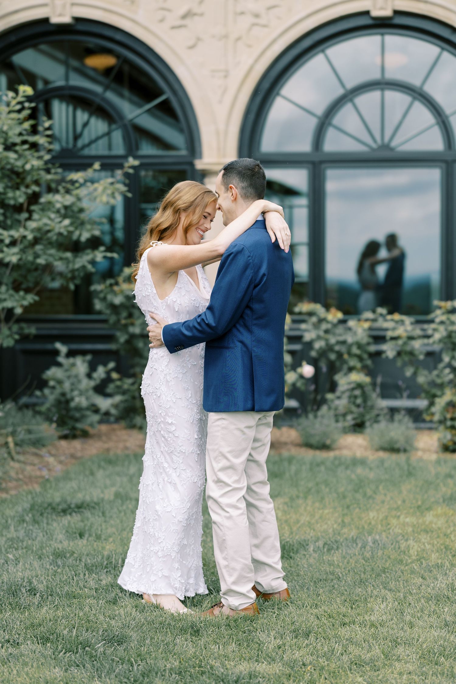 A sweet first look wedding moment captured on a garden lawn with elegant arched windows at Pendry Natirar in Peapack, NJ.