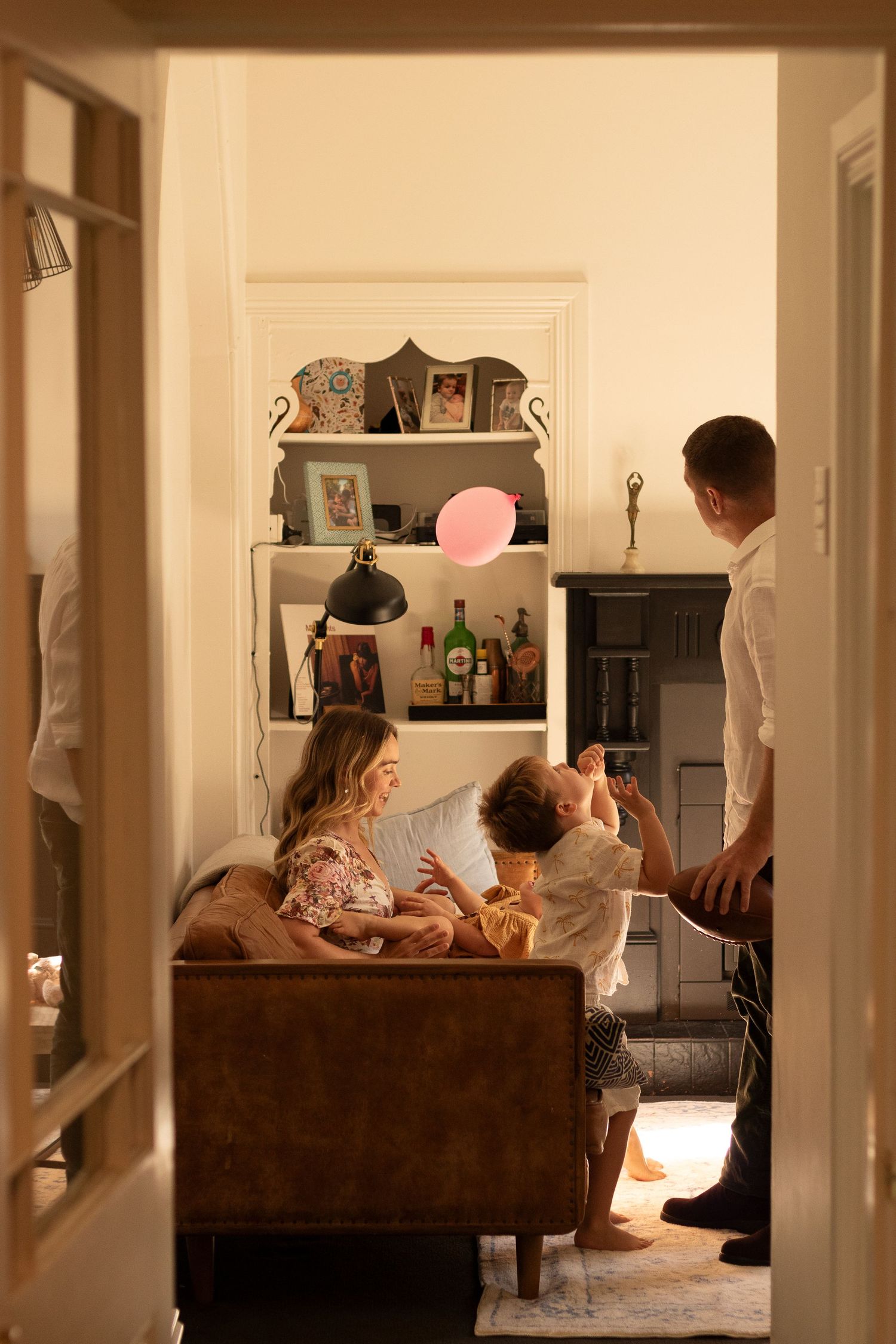 Family playing with balloon in cozy living room during evening golden hour.