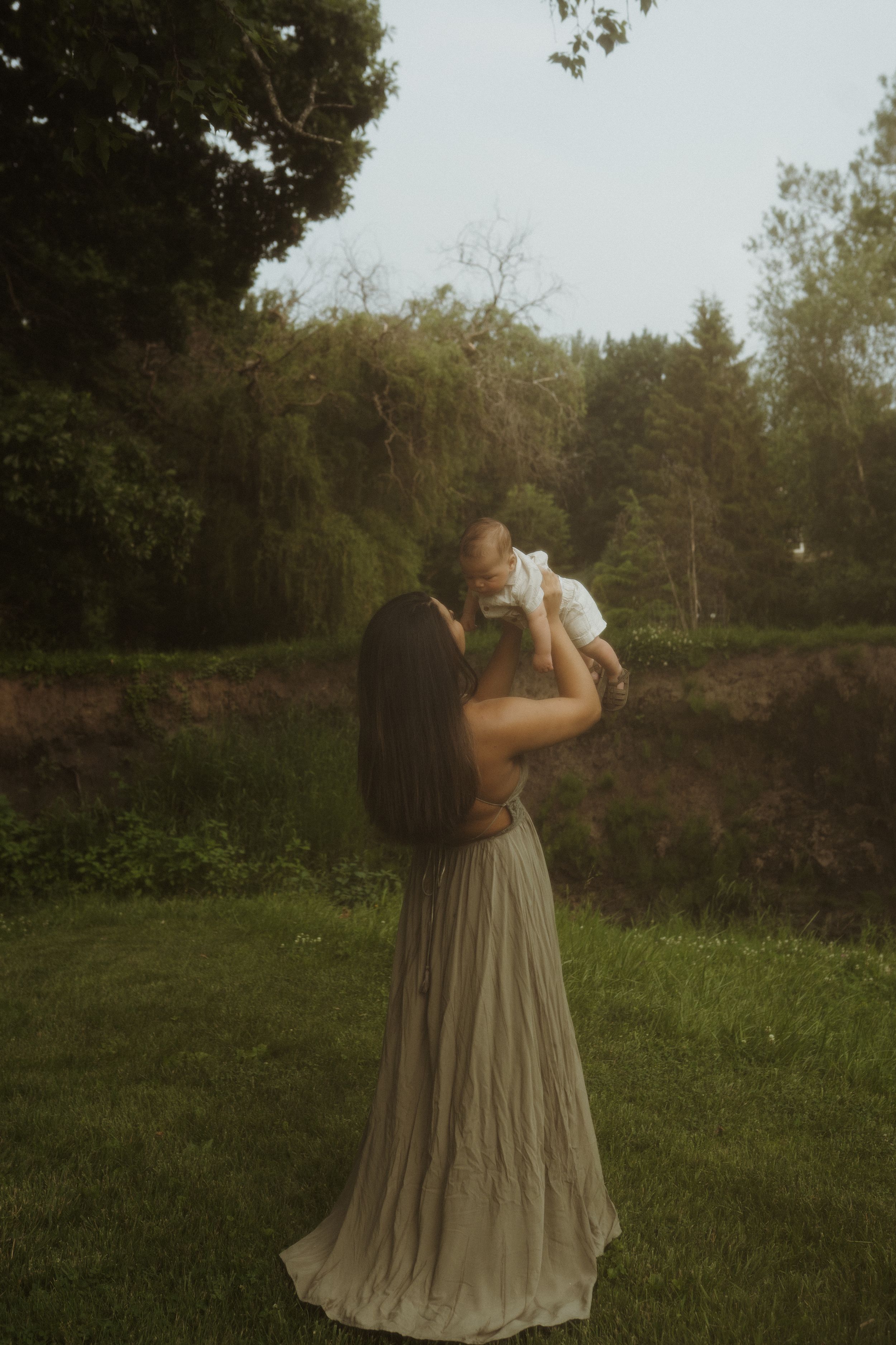 Someone in a flowing dress holds up a drink while standing in a grassy outdoor setting.