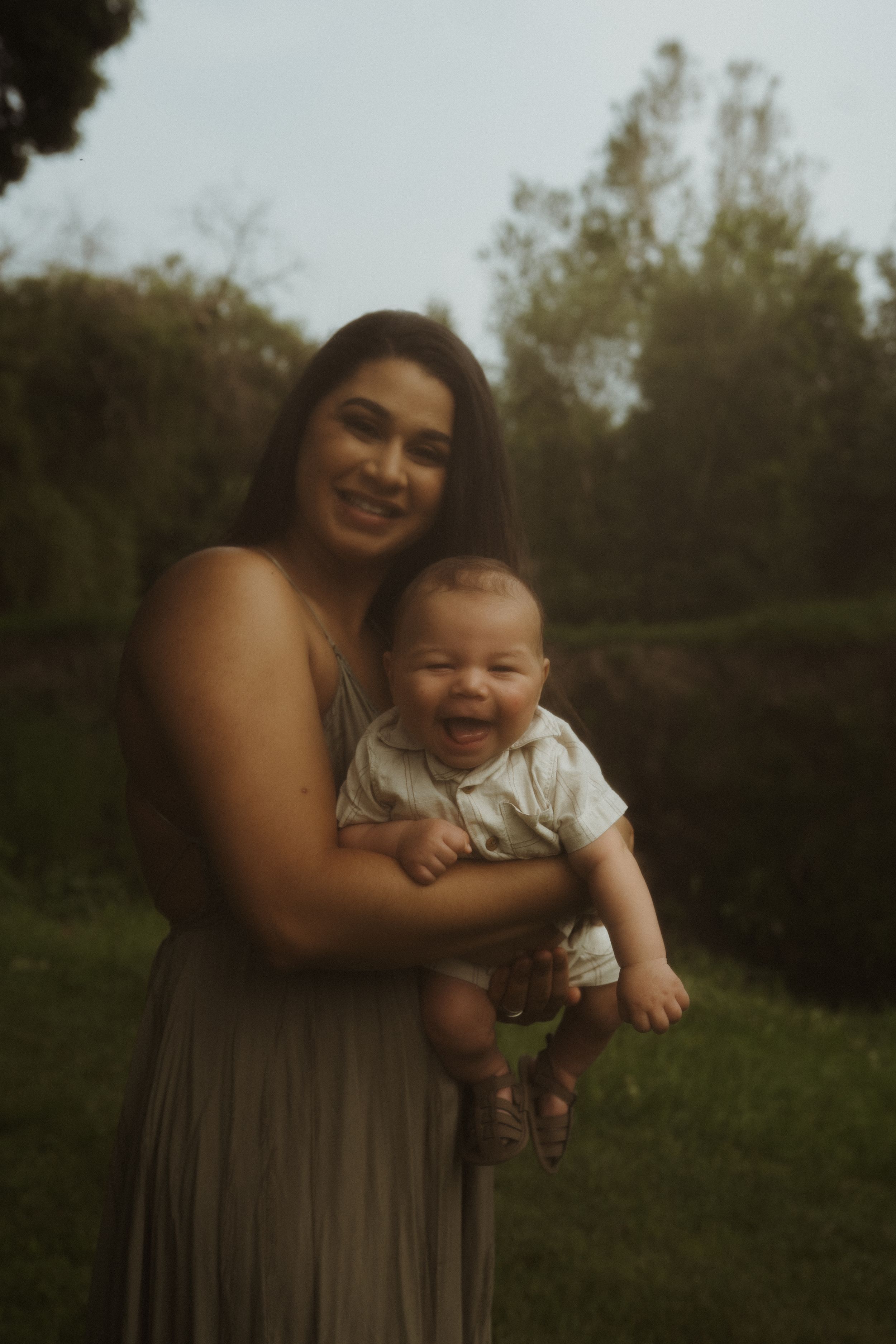 A heartwarming outdoor portrait showing a parent and baby sharing joyful smiles in a natural setting.