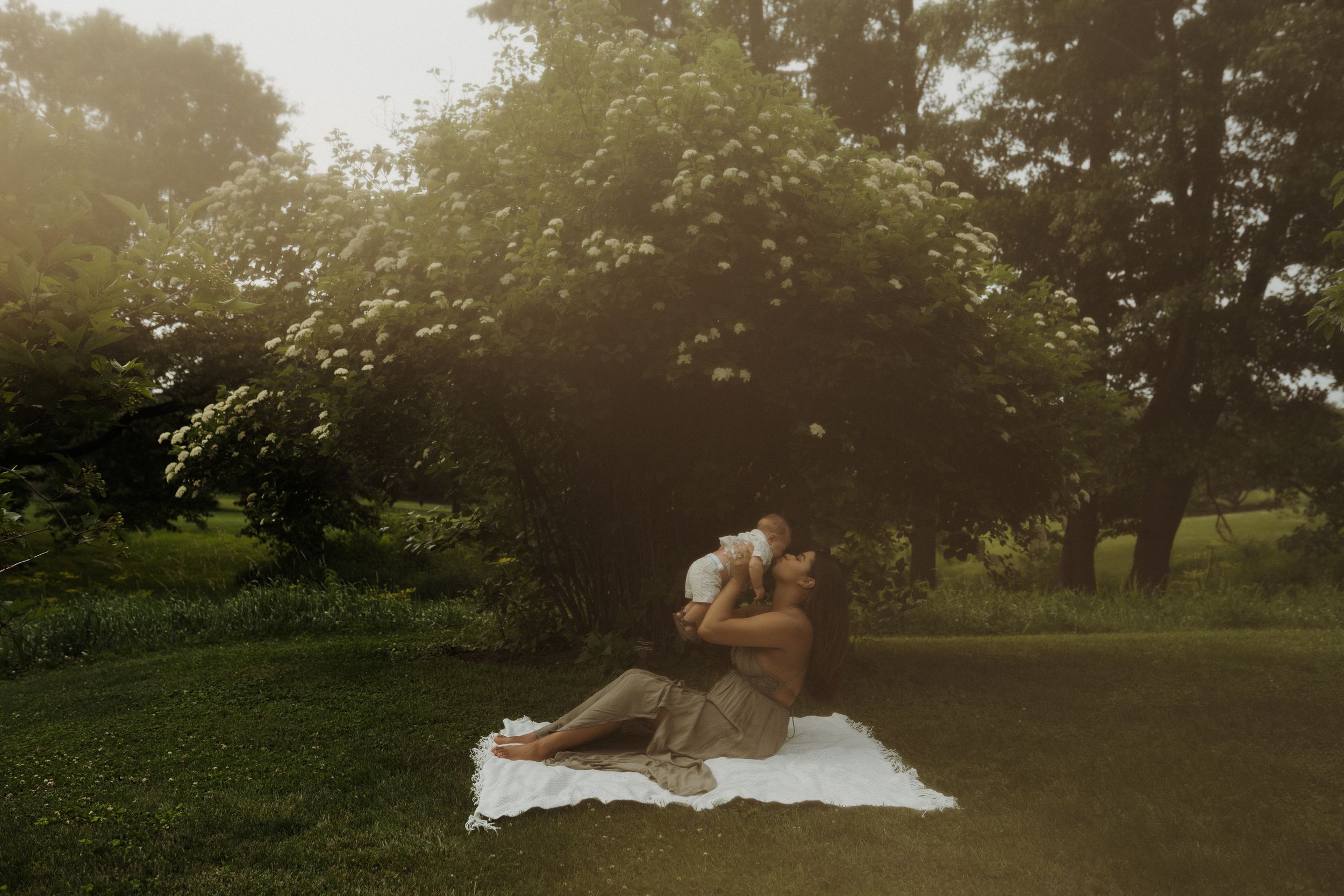 A romantic sunset photo of a couple embracing on a white blanket in a garden setting.