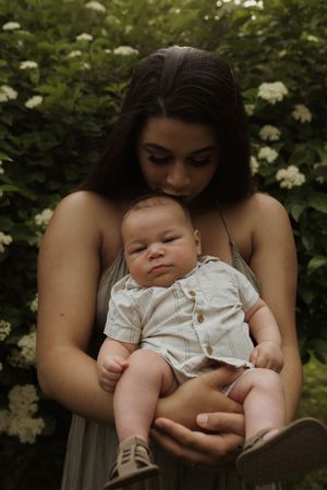 An intimate portrait of a parent cradling a baby against a backdrop of white flowering bushes.