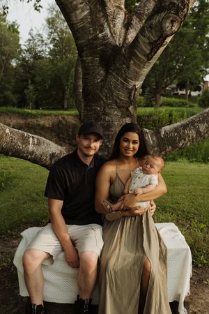A family portrait under a large birch tree with figures seated on a white blanket in a park setting.