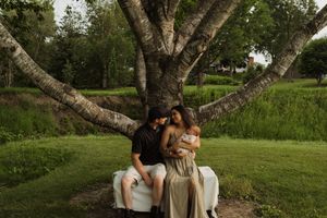 A couple shares an intimate moment while sitting under a branching birch tree on a summer evening.