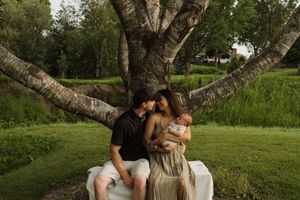 A tender moment captured between a couple seated beneath a sprawling birch tree in a park setting.