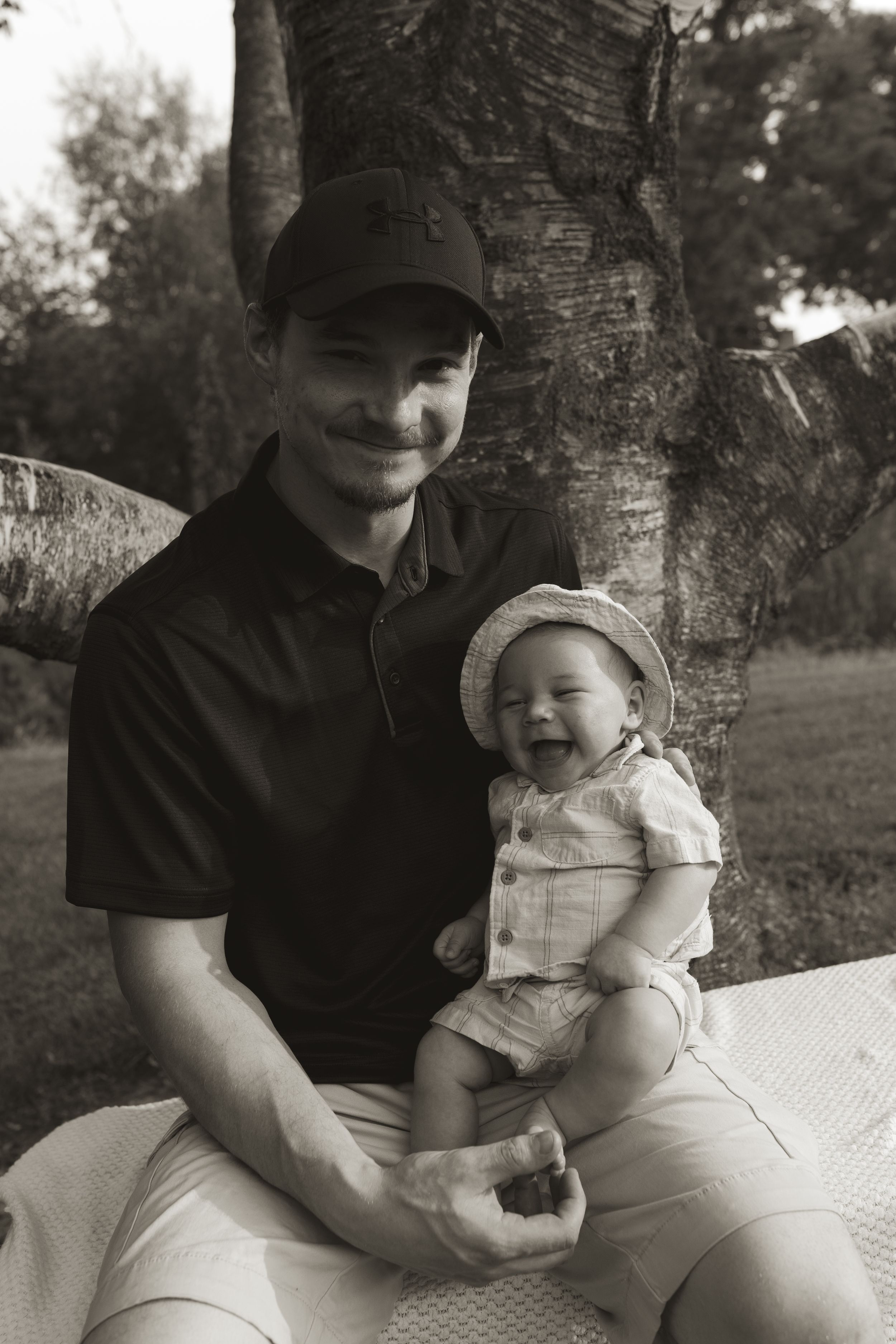 A black and white photo of a parent and baby sitting together by a tree.