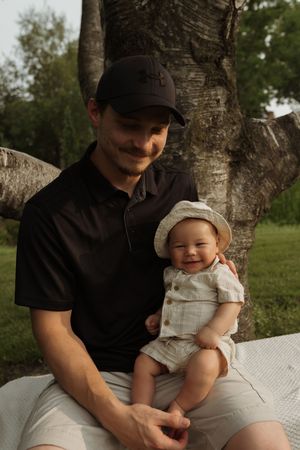 A parent and infant share a tender moment while sitting outdoors on a white blanket.