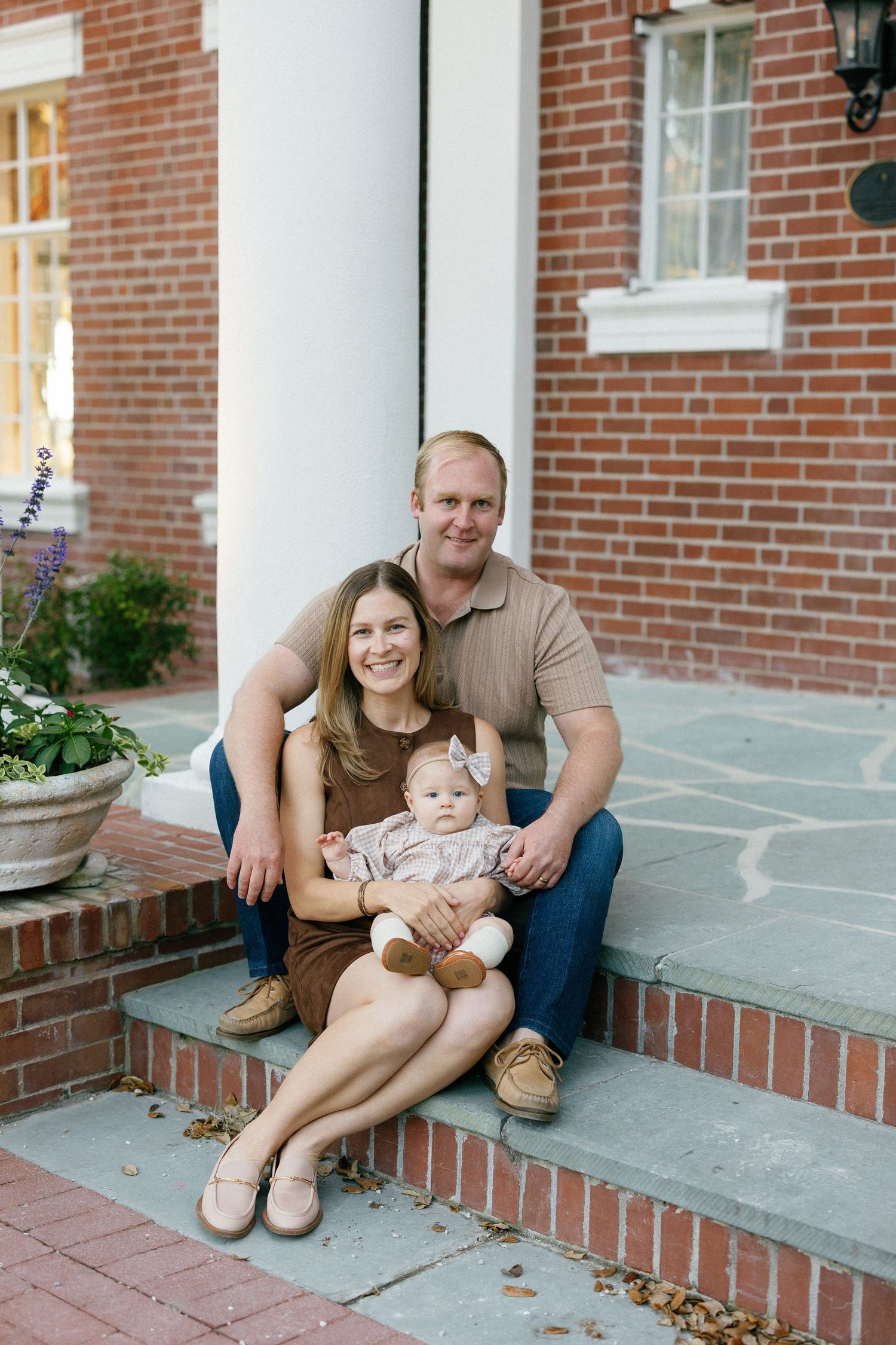A family shares a playful moment together while sitting on stone pavers near a brick building at sunset.