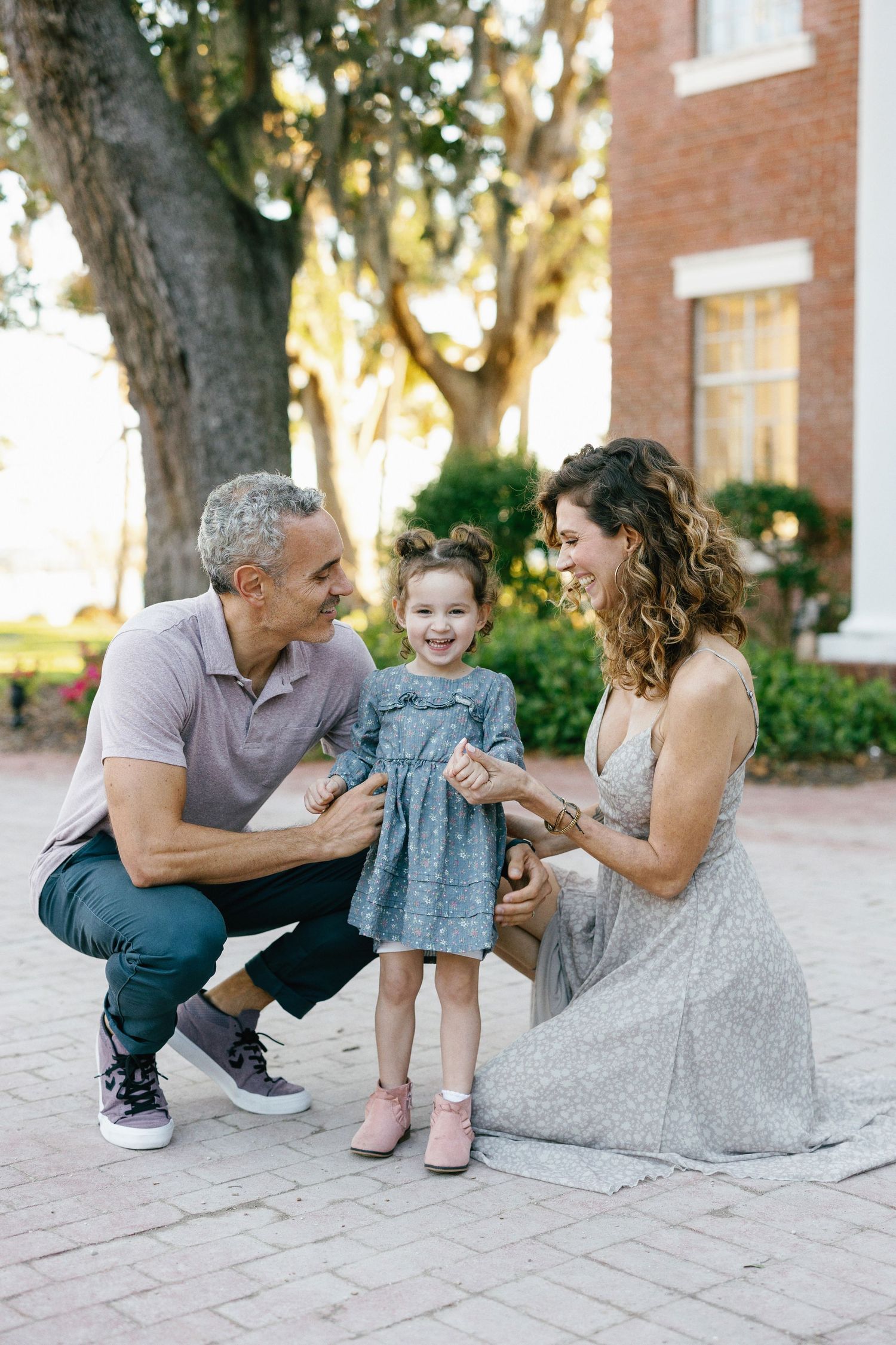 A family shares a playful moment together while sitting on stone pavers near a brick building at sunset.