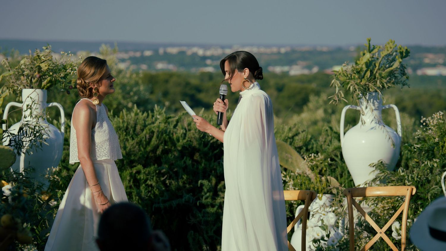 A remote ceremony setup on a rustic outdoor terrace overlooking a scenic countryside landscape at sunset.