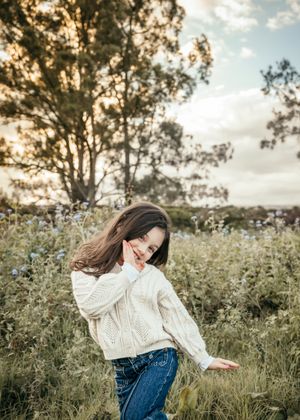 A cozy autumn scene shows someone in a cream knit sweater and jeans enjoying a peaceful moment in a wildflower field.