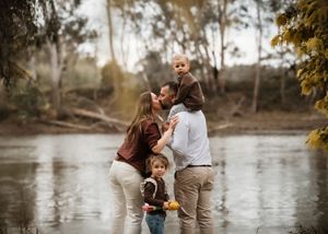 A family enjoys a playful autumn day together by the water's edge in matching brown and white outfits.