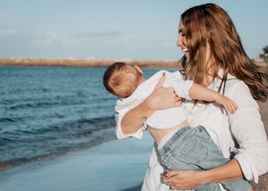 A tender moment shared between parent and child at the beach with blue ocean waters and sunlit scenery in the background.