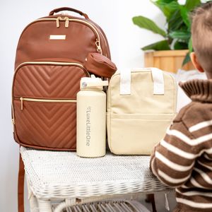 Brown diaper backpack with quilted pattern displayed with cream colored lunch bag and stainless steel water bottle.