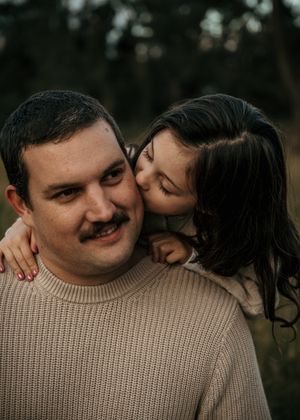 A tender moment captured outdoors showing affection between two people in soft natural lighting.