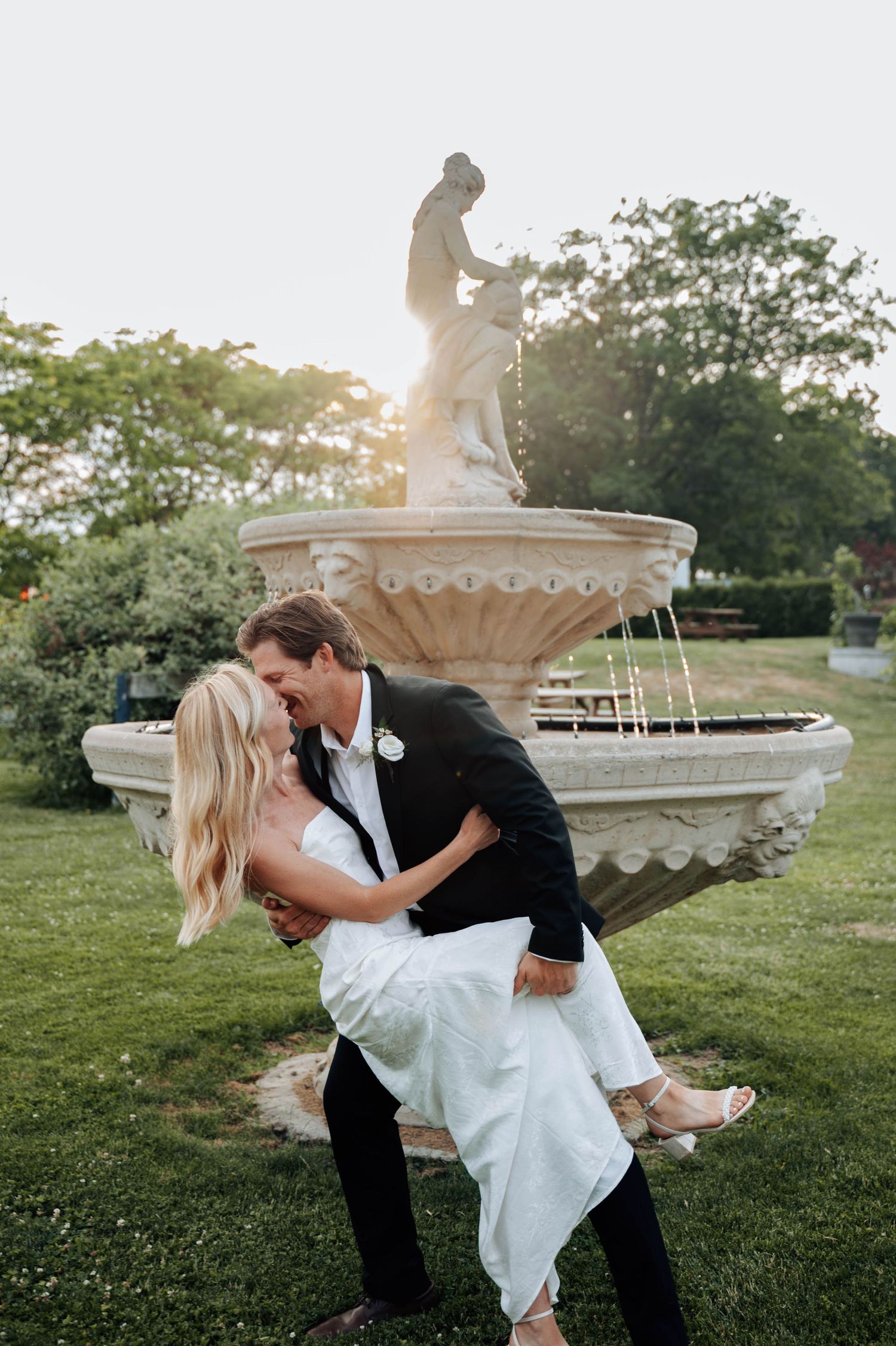 Romantic couple dances outdoors at sunset with elegant fountain in the background.