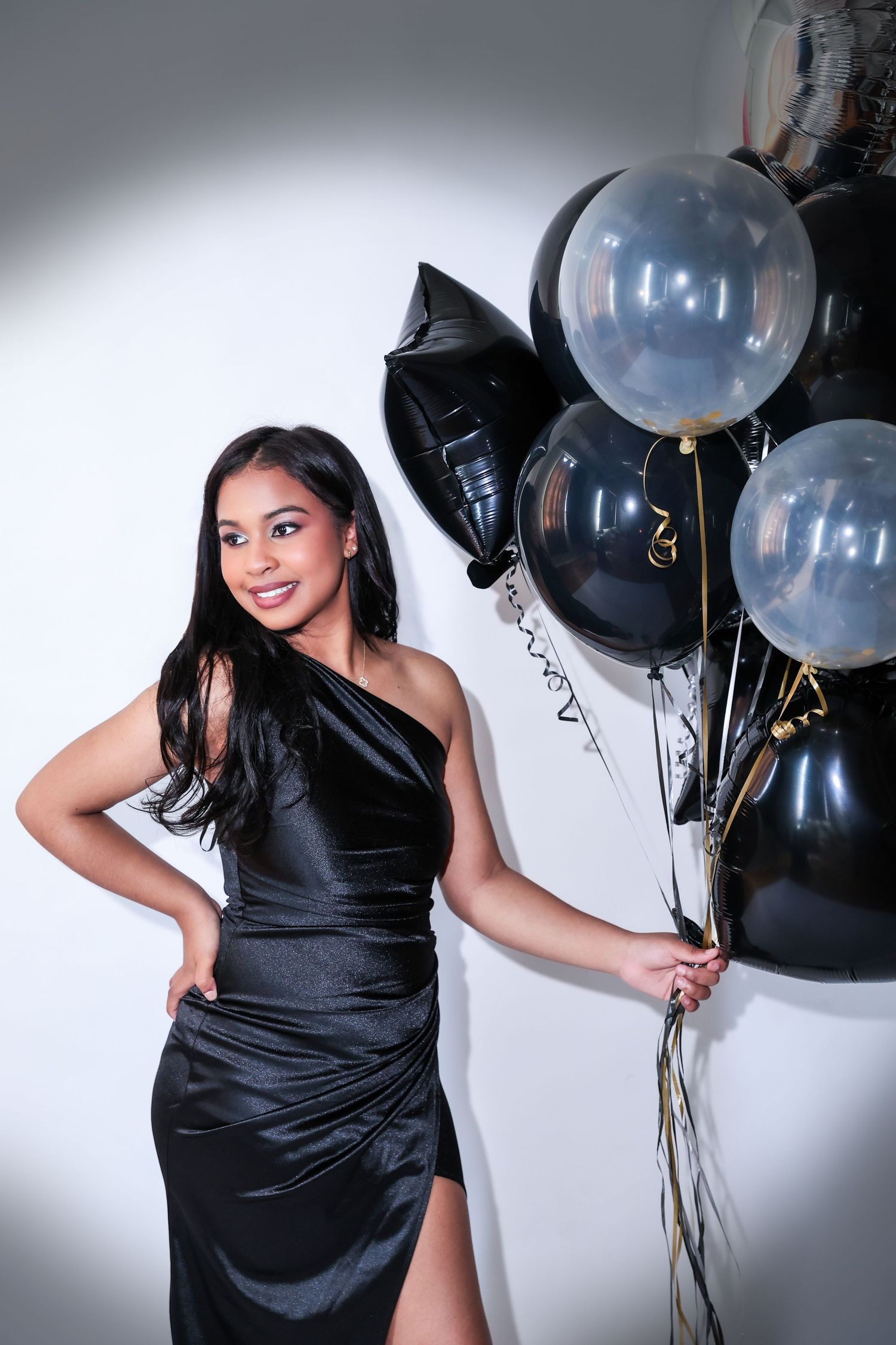 An elegant black dress photoshoot with balloons against a white studio backdrop.