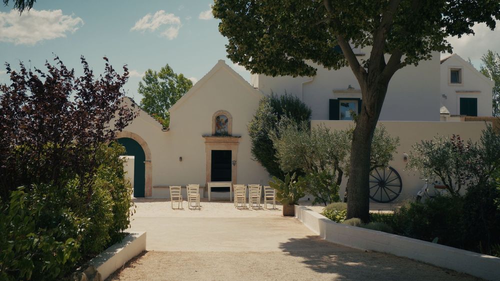 A panoramic view of a rustic countryside villa with white walls, trees and a blue summer sky in Italy.