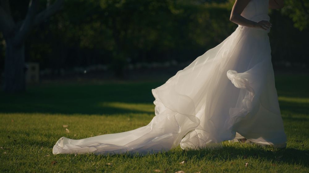 Wedding dress train trails elegantly across lush green grass creating a sweeping romantic effect in outdoor setting.