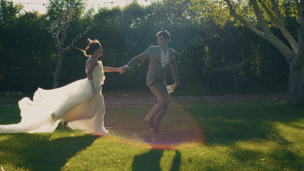 A couple dances joyfully in a sunlit garden as a flowing white dress catches the golden evening light.
